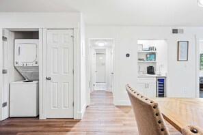 A kitchen with white appliances, a dining area with a wooden table and a chair, and a hallway leading to another room. - Family-friendly condo with top-floor balcony, complex pools, tennis, pickleball (Hilton Head)