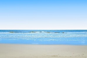 A beach with clear blue water and a sandy shore. - Family-friendly condo with top-floor balcony, complex pools, tennis, pickleball (Hilton Head)