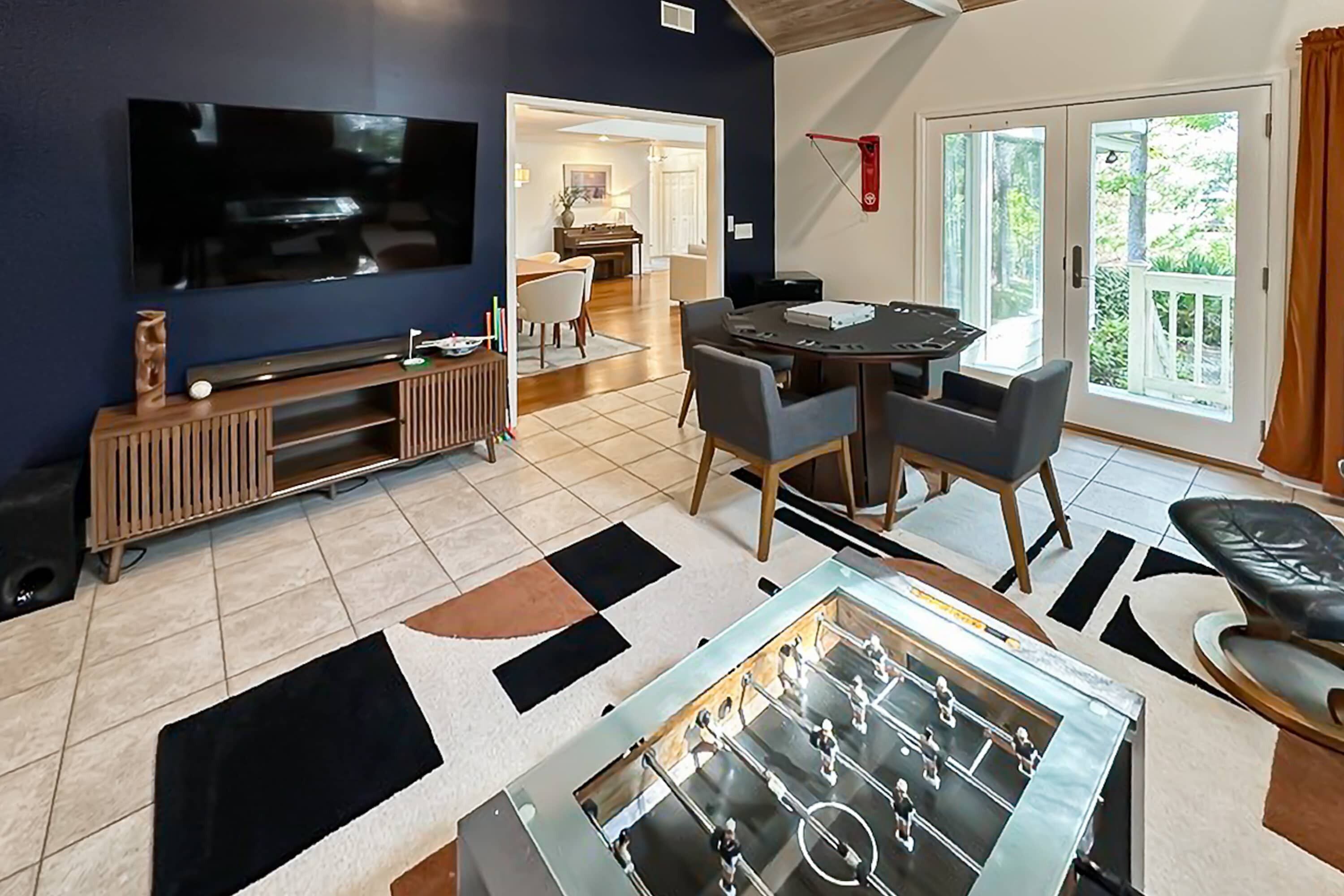 A living room with a foosball table, a TV, and a dining area with chairs.
