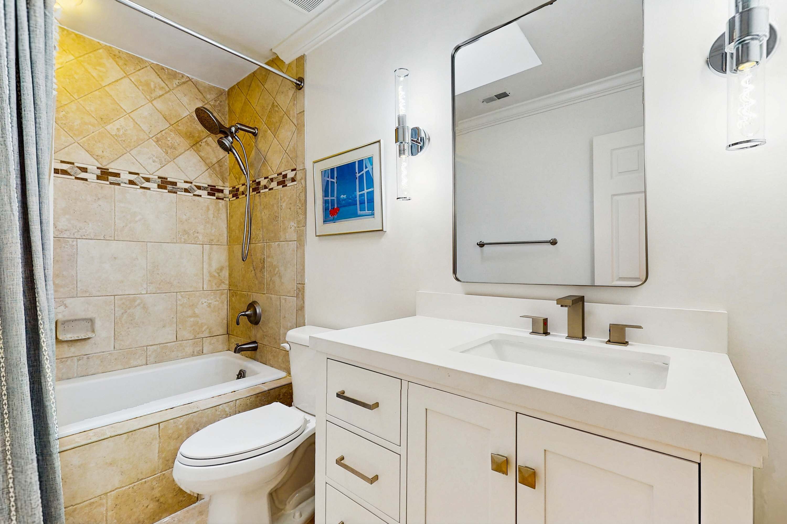 A bathroom with a bathtub, toilet, and sink, featuring a tiled shower area and a framed picture on the wall.