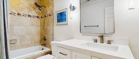 A bathroom with a bathtub, toilet, and sink, featuring a tiled shower area and a framed picture on the wall.