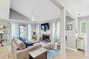 Ein modernes Wohnzimmer mit einer Couch, einem Hocker, einem Kamin, einem Fernseher und Vorhängen.