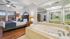 A bedroom with a bed, bedside table, lamp, and a large mirror. - 🌲 Baskins Creek 109 - Walk to Downtown - Cozy Fireplace 🌲 (Gatlinburg)
