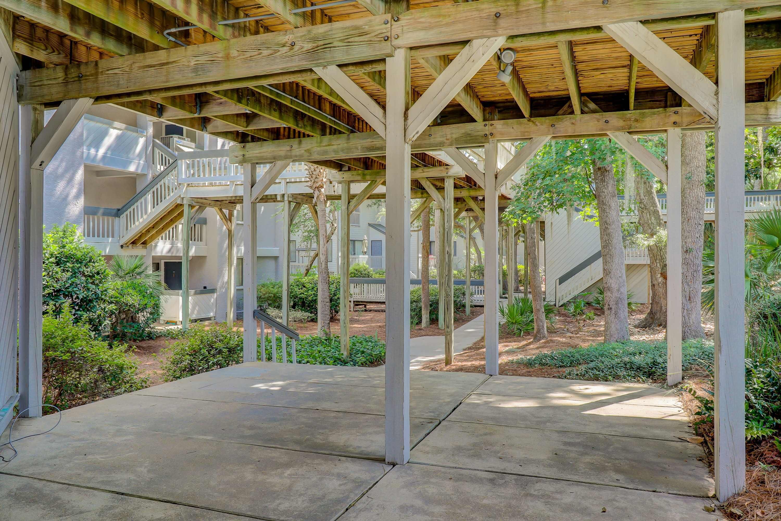 A covered outdoor area with a concrete floor, wooden beams, and a staircase leading to an upper level.