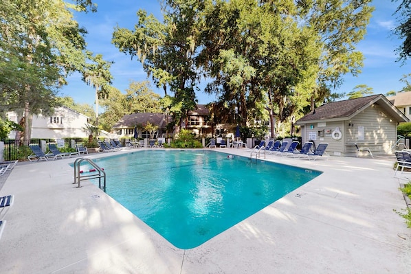 A rectangular swimming pool with a metal ladder, surrounded by lounge chairs and trees. - Pool view condo with screened in patio, complex pool hot tub, near golf (Hilton Head)
