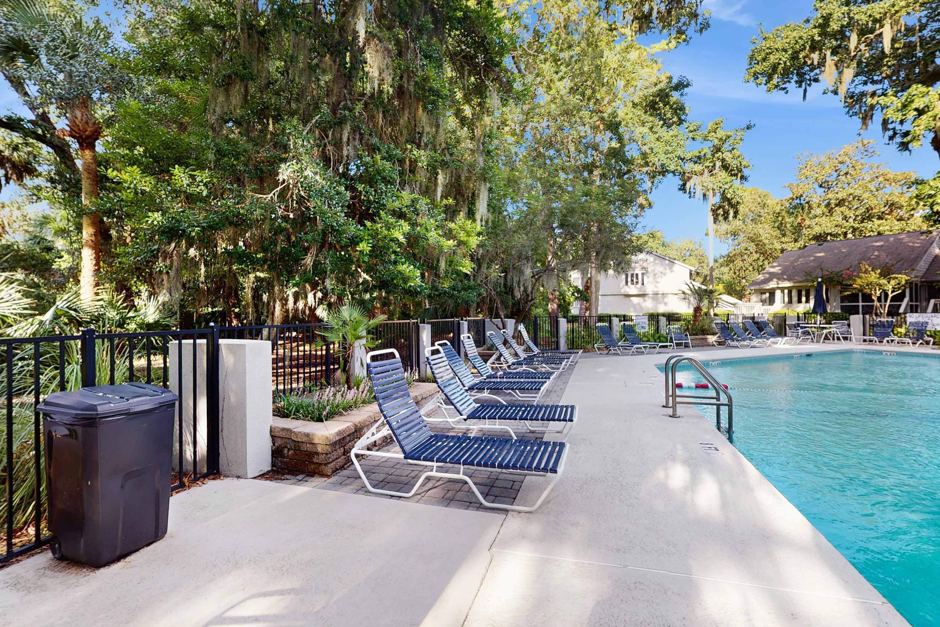 Un espace aménagé au bord de la piscine, avec des chaises longues, une piscine et une clôture.