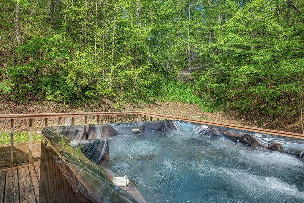 A hot tub surrounded by a wooden deck and forest. - Escape to the serene beauty of the Smoky Mountains, Shiner's Hollow. (Gatlinburg)