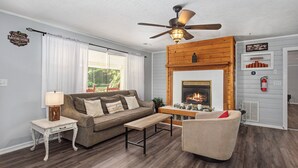 Un salon comprenant un canapé, une table basse, une cheminée, un ventilateur de plafond et une table d’appoint avec une lampe.