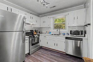 A kitchen with white cabinets, stainless steel appliances, a window with blinds, and a wooden floor. - Escape to the serene beauty of the Smoky Mountains, Shiner's Hollow. (Gatlinburg)