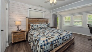 Une chambre à coucher comprenant un lit, une table de chevet, une lampe, un ventilateur de plafond et une fenêtre avec des stores.