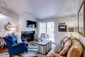 A living room with a blue armchair, a fireplace, a television, and a large window.