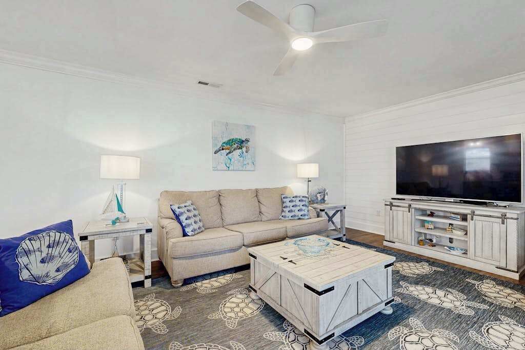 A living room with a beige sofa, a coffee table, a TV, and a ceiling fan.