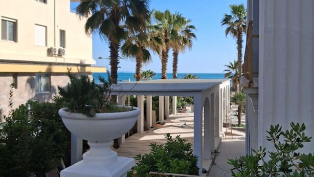 A corridor with a view of the sea, palm trees, and a building with balconies. - Divine Apartment by TOK (Durrës)