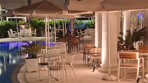 An indoor pool area with lounge chairs and umbrellas, surrounded by columns and potted plants. - Divine Apartment by TOK (Durrës)