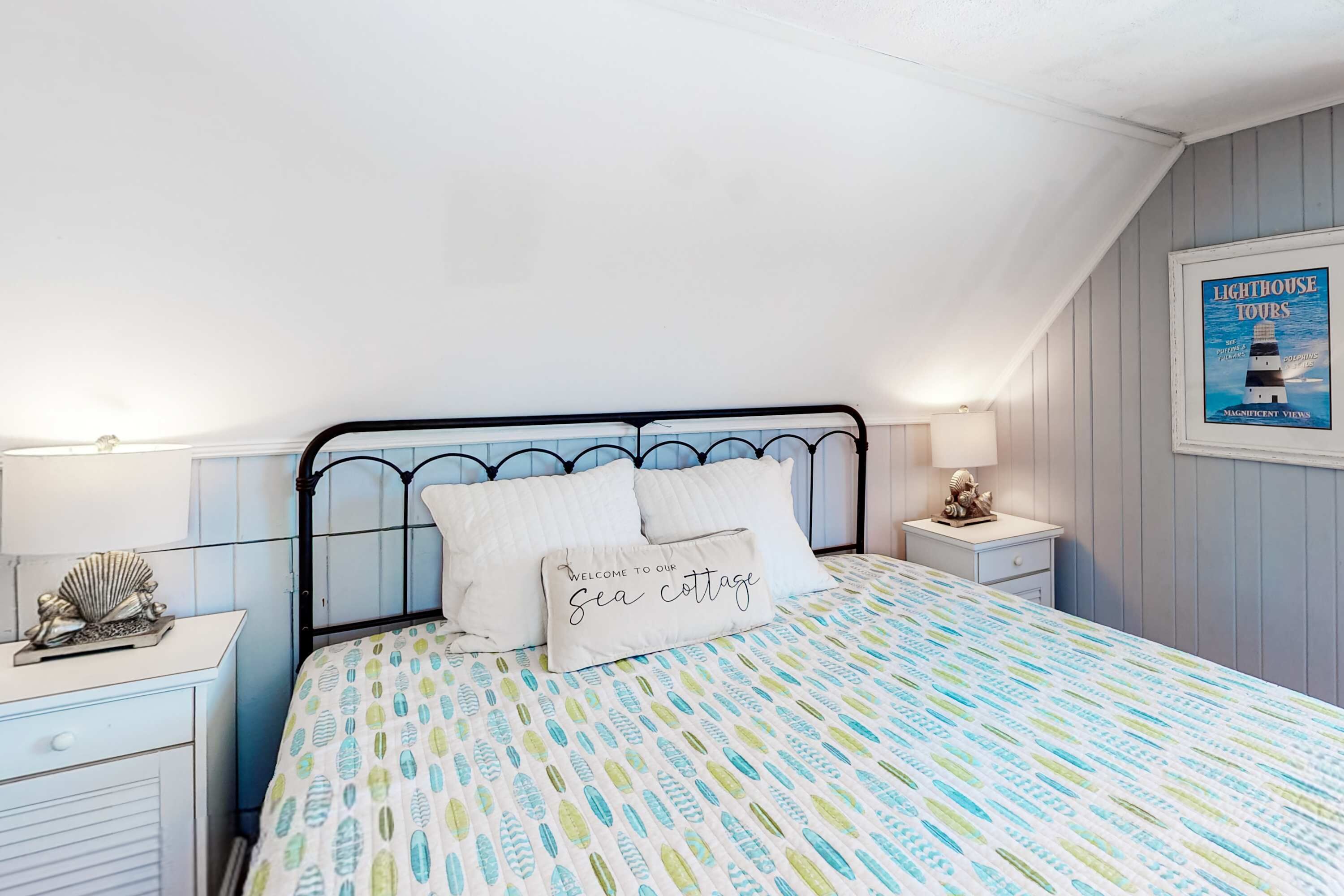 Une chambre à coucher comprenant un lit, deux tables de chevet, une commode, une affiche accrochée au mur et un plafond à pente.