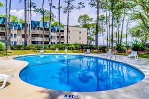 A swimming pool with a 8 ft no diving sign, surrounded by lounge chairs and tall trees.