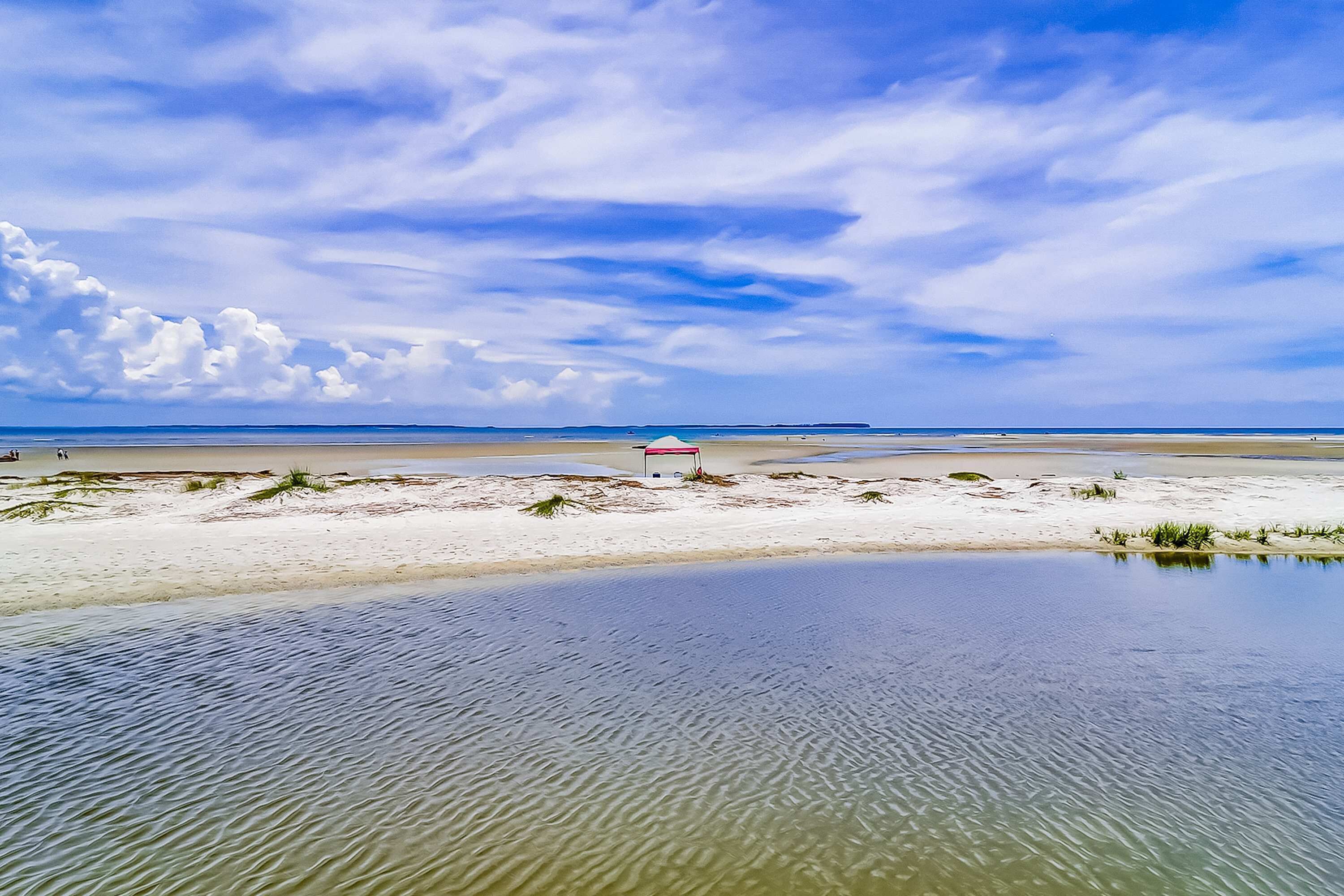 A beach with a clear sky, calm water, and a small structure with a red roof.