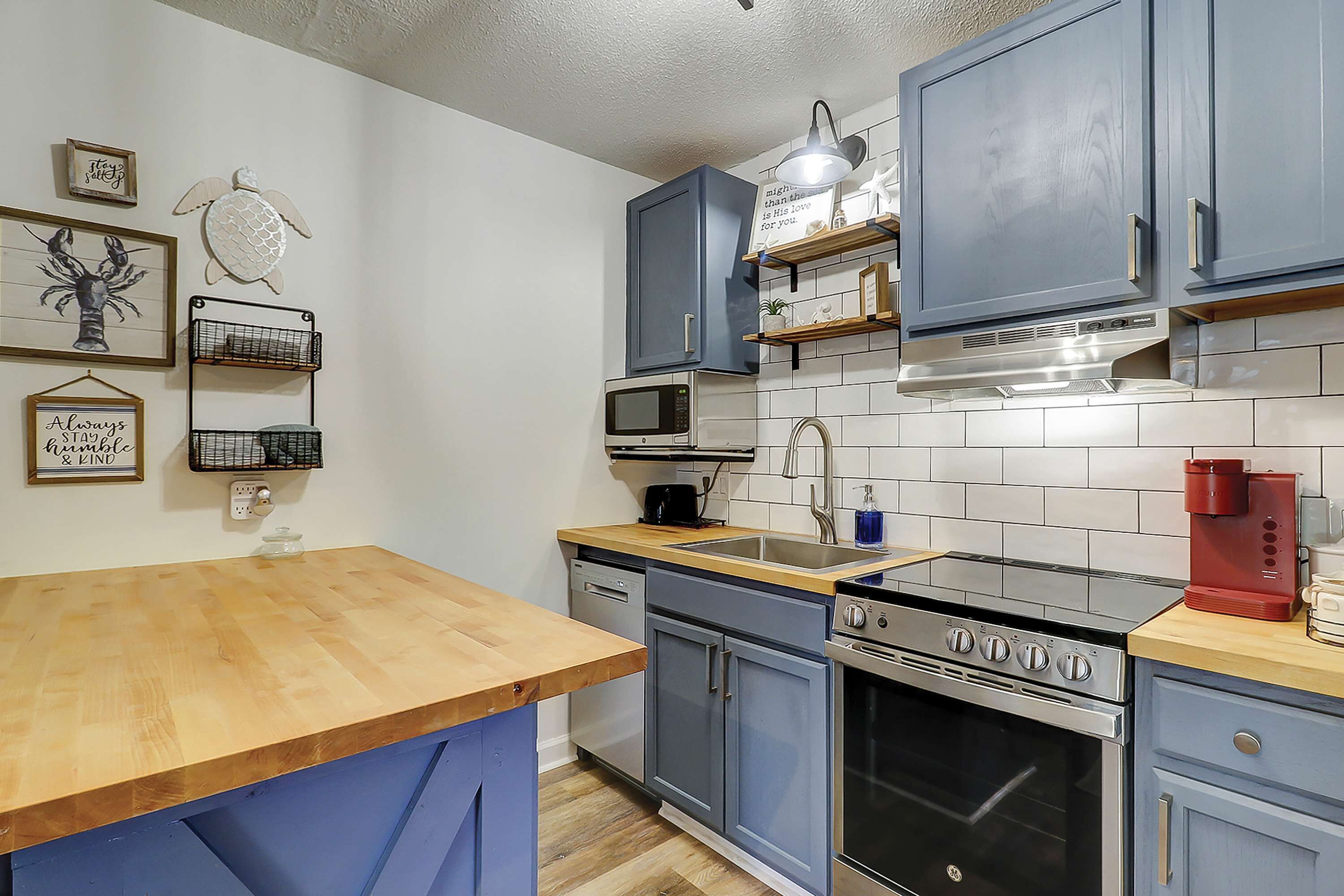 A kitchen with blue cabinets, a wooden countertop, a microwave, an oven, and a coffee maker.