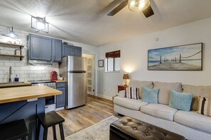 A compact kitchen with modern appliances, a wooden dining table, and a sofa in a living area.