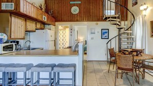 A kitchen with wooden cabinets, a central island with bar stools, a dining area with wicker chairs, and a spiral staircase. - Top-floor villa with fairway views - central AC, private W/D, WiFi - Dogs OK (Edisto Beach)