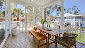 Une terrasse extérieure couverte, avec une table et des bancs en bois, de grands pots de plantes et une vue sur les maisons voisines.