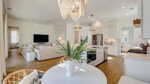 Un salon moderne doté d’un téléviseur à écran plat, d’une table à manger agrémentée d’une plante en pot et d’un coin cuisine avec des meubles blancs et une cuisinière.