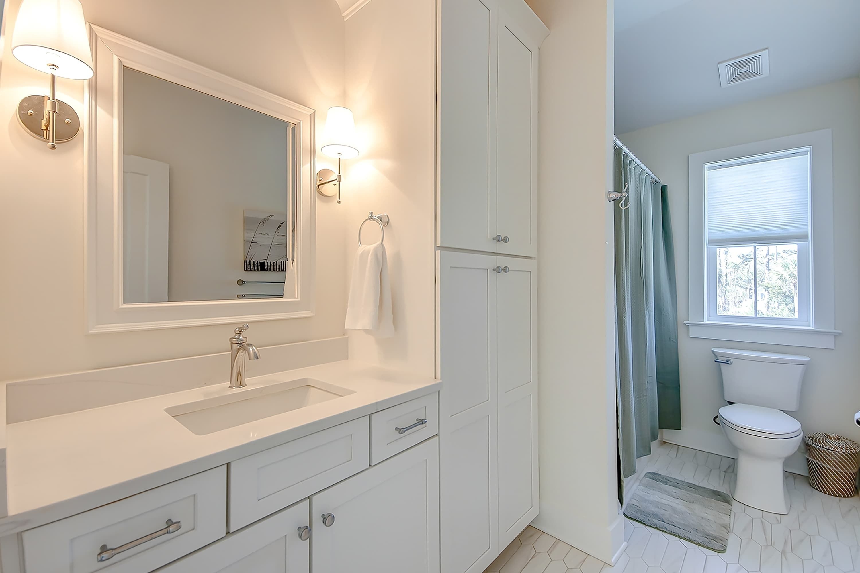 A bathroom with a white sink, mirror, and cabinet, a toilet, and a shower area.