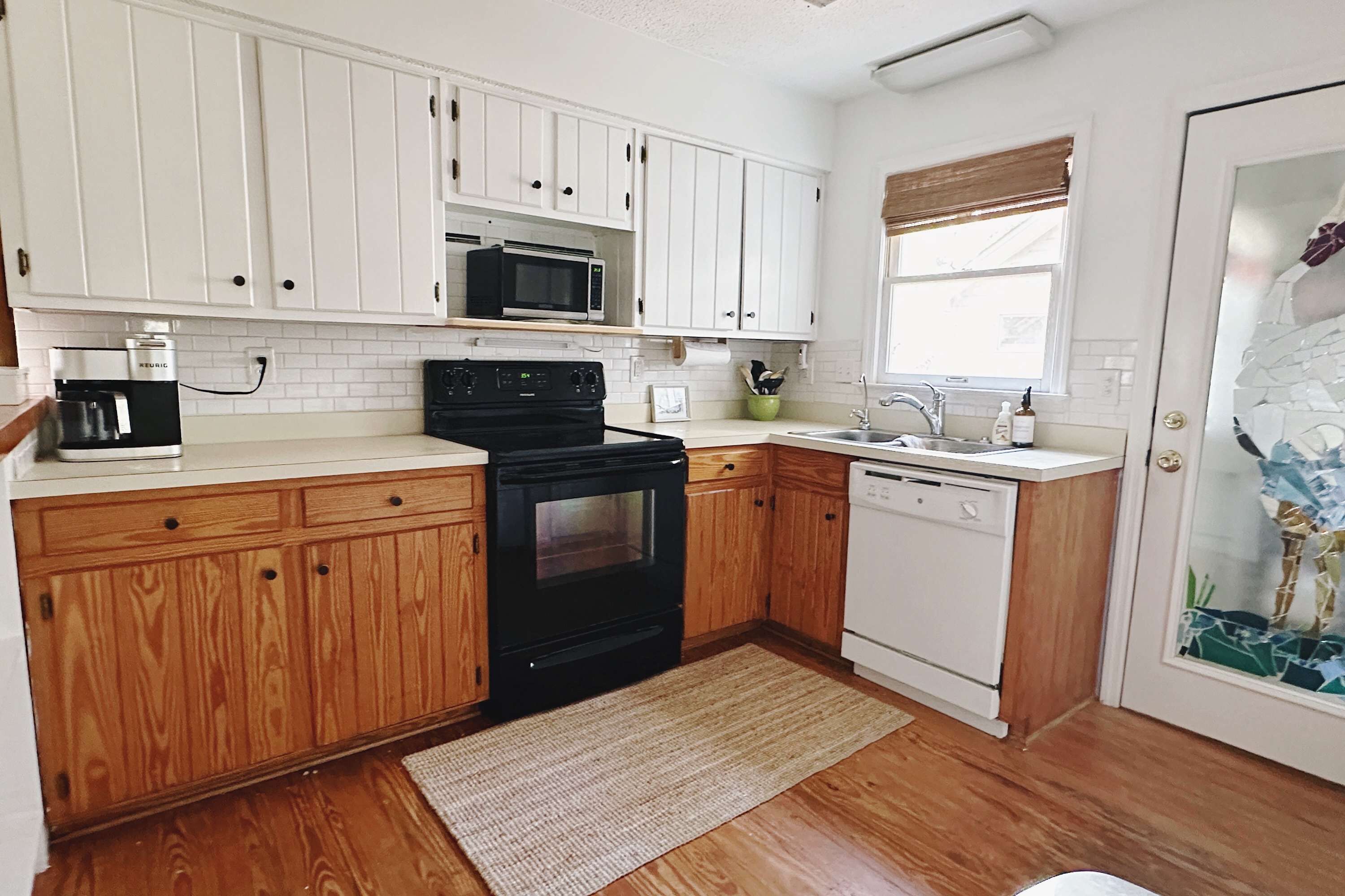A kitchen with white cabinets, a black stove, a microwave, a dishwasher, and a window with blinds.