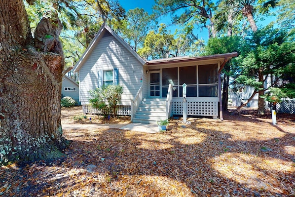 A house with a porch, a screened area, and a yard with trees and fallen leaves.