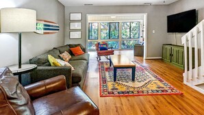 A living room with a sofa, a leather chair, a coffee table, a patterned rug, a lamp, and a television. - Vibrant, Waterfront Home with Free WiFi, Full Kitchen, Gas Grill, & A/C (Edisto Beach)