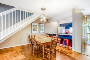 A dining area with a wooden table and chairs, a kitchen with blue cabinets, and a staircase.