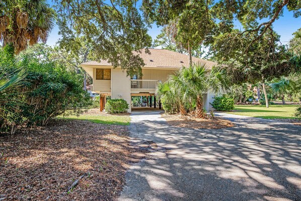 A two-story house with a front porch, surrounded by dense foliage and a well-maintained lawn.