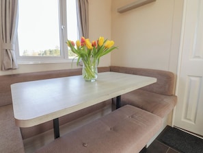 A room with a white table, brown cushioned bench seating, and a vase with yellow tulips. - Cornholme Lodge (Accrington)