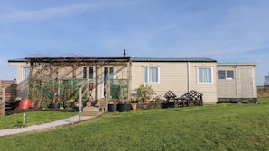 Une maison mobile de plain-pied, dotée d’un porche, de plantes en pot et d’un petit jardin.