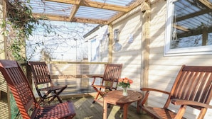 Une terrasse en bois avec quatre chaises et une table, une porte vitrée et un mur en bois.