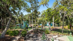 An outdoor patio area with tables and chairs, surrounded by trees and a playground. - Spacious home near beach with access to resort amenities & free state park entry (Edisto Beach)