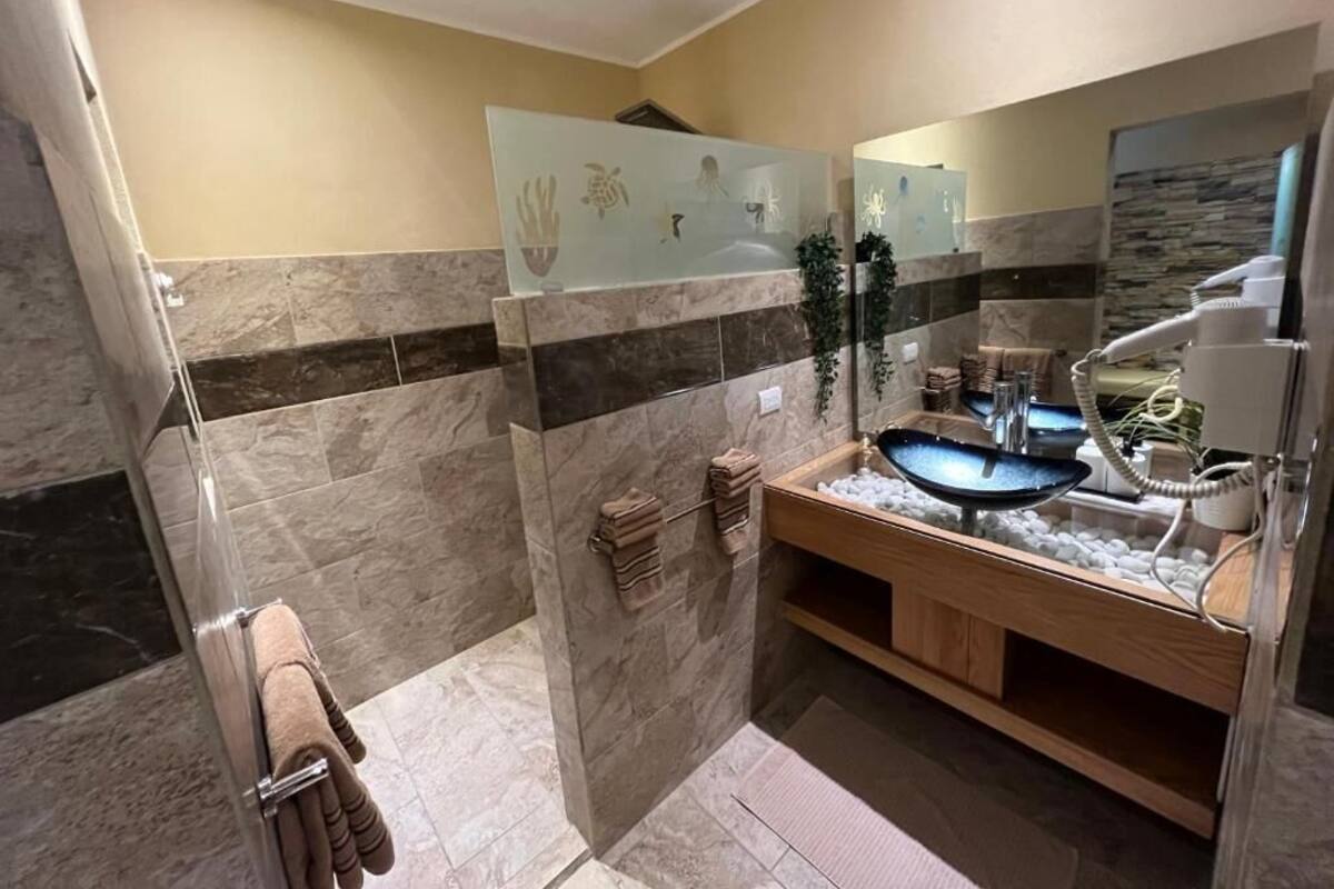 A bathroom with a glass shower enclosure, a sink with a marble countertop, and a towel rack with towels.