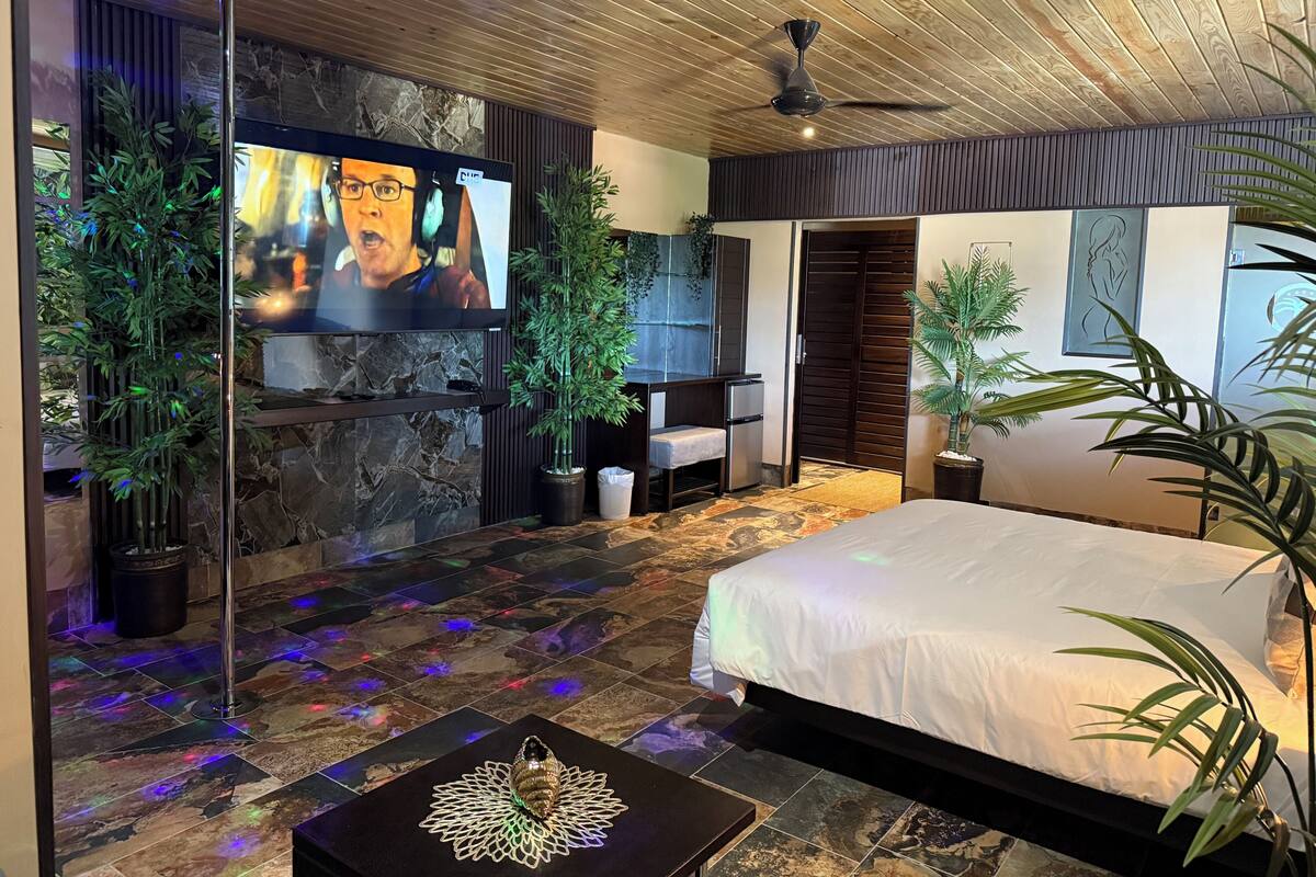 A modern bedroom with a bed, television, potted plants, and a stone wall.