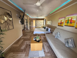 A modern hotel room with a wooden herringbone floor, a sofa, a bed, a coffee table, and artwork on the walls. - Sosua Inn Hotel (Sosúa)