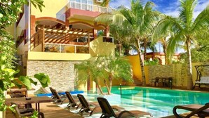 Un espace aménagé au bord de la piscine, avec des chaises longues, une piscine et un bâtiment doté de balcons et de palmiers.