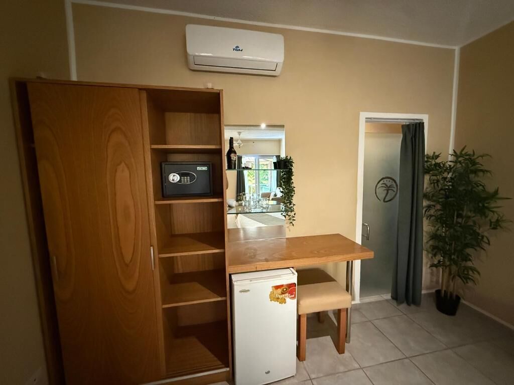 A compact kitchen with a wooden cabinet, a small refrigerator, a countertop, and a potted plant.
