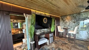 Un intérieur moderne avec un mur en pierre, un téléviseur à écran plat, un petit coin salon et un plafond en bois.