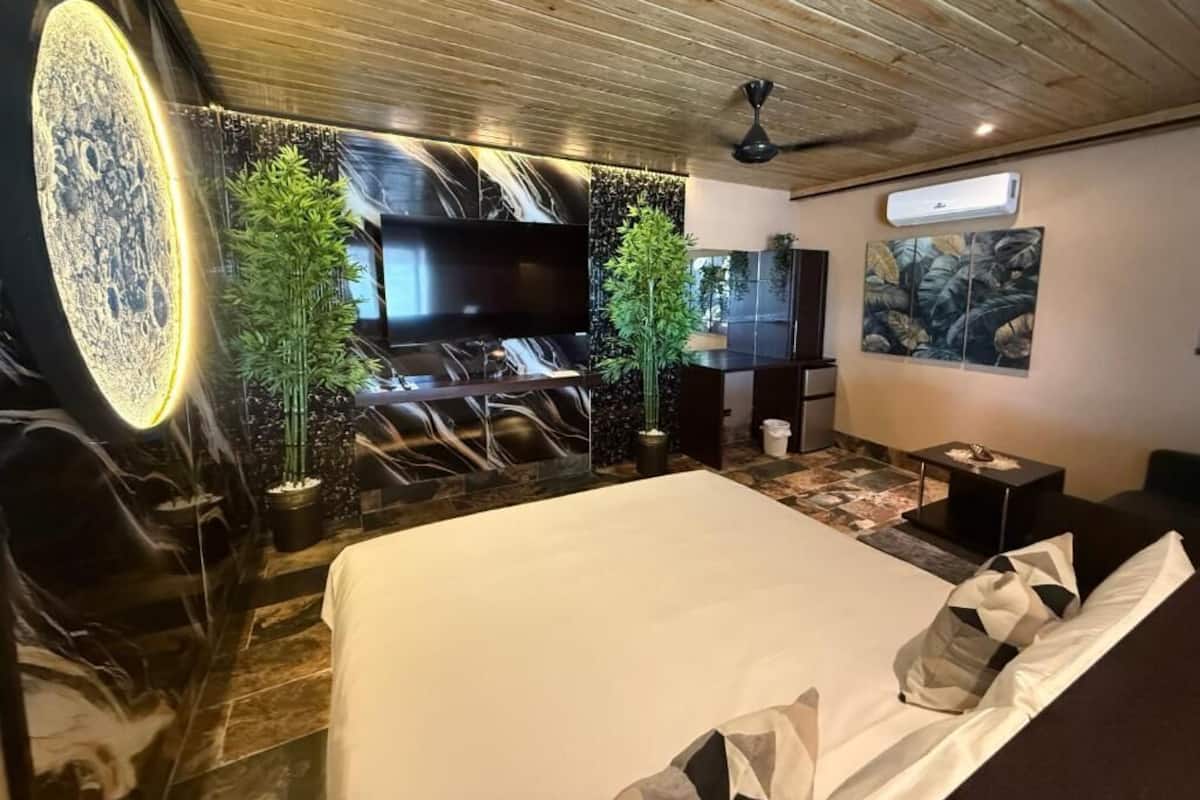 A modern hotel room with a large bed, a flat-screen TV, a ceiling fan, and a wall-mounted TV.