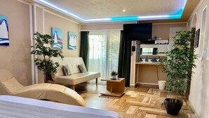 Une chambre d’hôtel avec un lit, un canapé, une télévision, une petite table et une plante en pot.