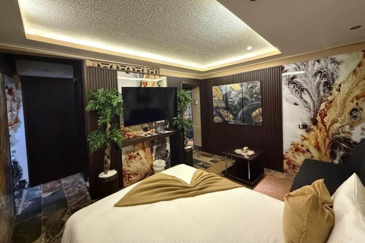 A modern hotel room with a large bed, a flat-screen TV, a small side table, and a decorative wall.