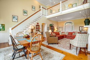 A spacious living area with a dining table, chairs, a sofa, and a staircase leading to an upper level. - Charming Home w/ Lagoon View, WiFi, Laundry, Central AC - Walk to the Beach (Edisto Beach)