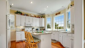 A kitchen with white cabinets, a central island with bar stools, a microwave, and a large window. - Charming Home w/ Lagoon View, WiFi, Laundry, Central AC - Walk to the Beach (Edisto Beach)