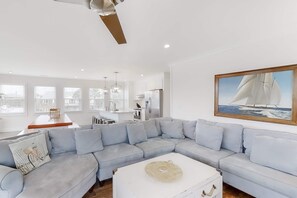 A modern living room with a light grey sectional sofa, a white coffee table, and a sailboat painting on the wall. - Bright, Modern Home 1 Block From Beach w/ AC, WiFi, W/D, Balcony (Edisto Beach)