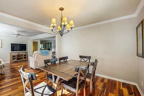 A dining area with a wooden table and chairs, a chandelier, and a television in the background. - Spacious house w/ deck, W/D, central location + walking distance to beach (Edisto Beach)