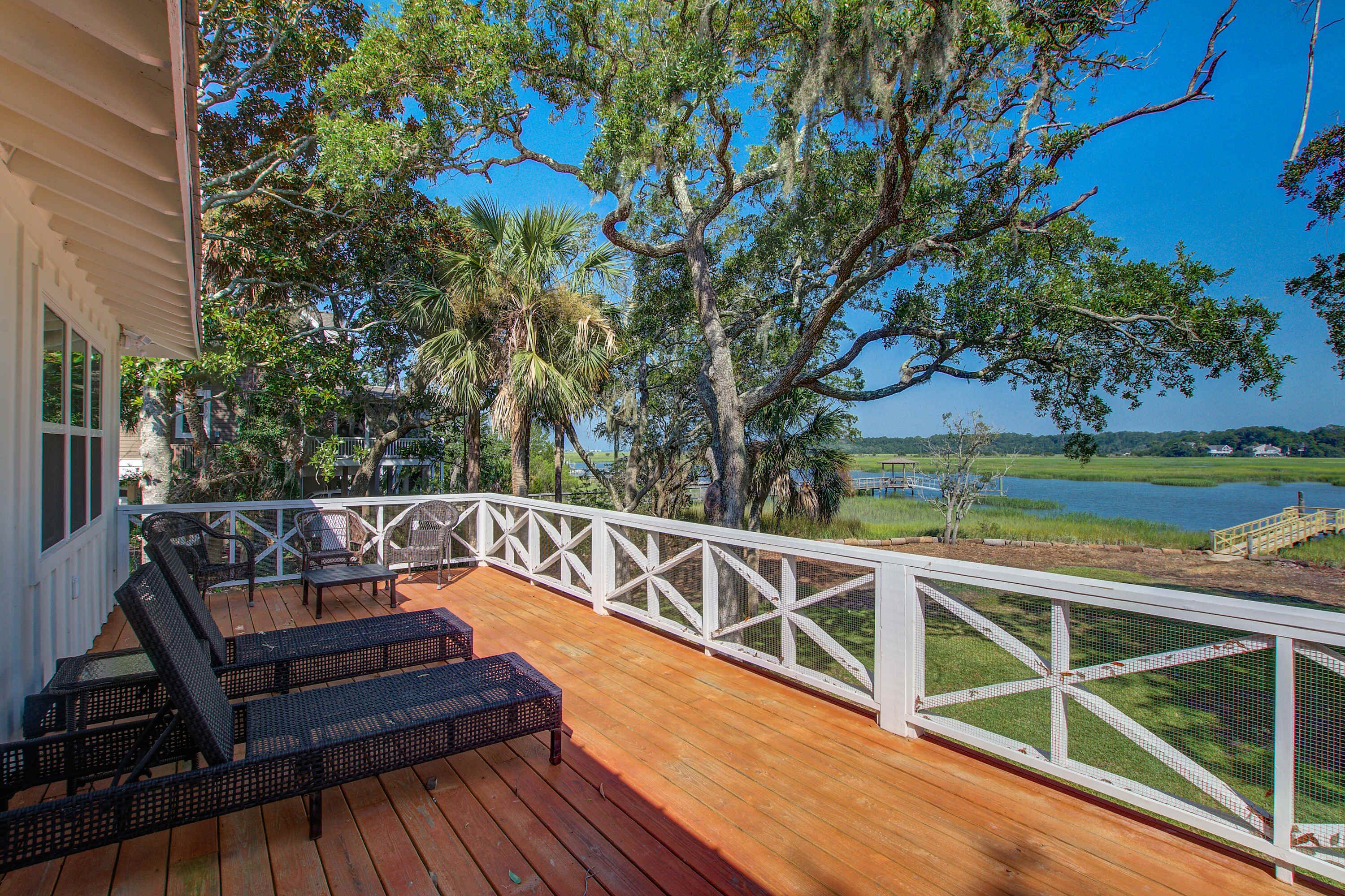 A wooden deck with outdoor furniture, a white railing, and a view of a lake and trees.
